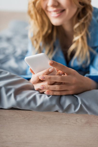 cropped view of cheerful woman chatting on smartphone while lying on bed in modern apartment  - Foto, Bild