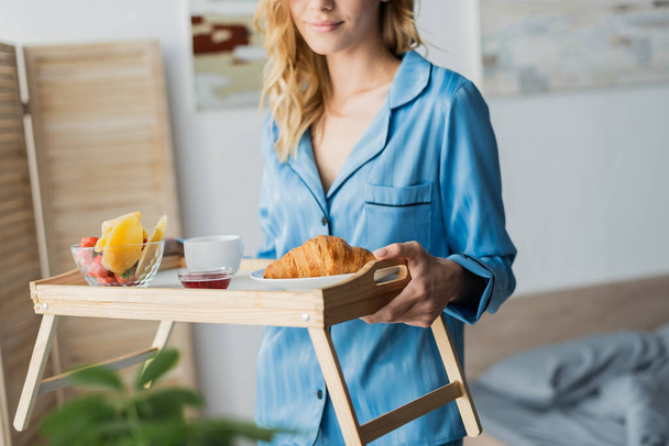 Mavi pijamalı, elinde kahvaltı tepsisi olan mutlu bir kadın manzarası.  - Fotoğraf, Görsel