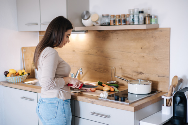A young beautiful woman is preparing lunch in her kitchen at home. High quality photo - Zdjęcie, obraz