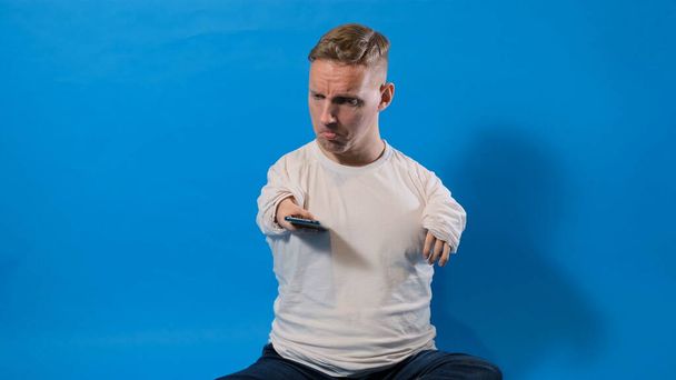a man with disabilities looks with surprise at the smartphone screen on an isolated blue background - Фото, зображення
