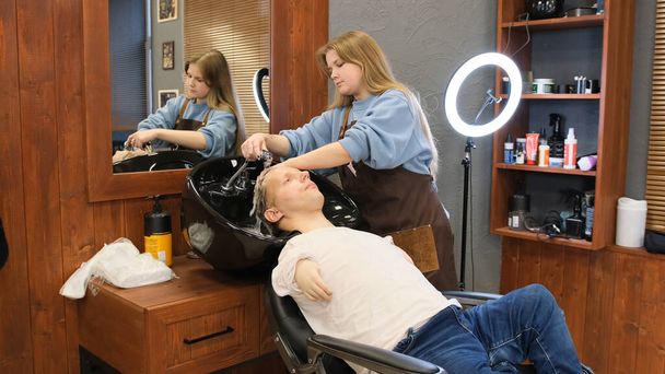 Перукарня миє волосся чоловіка з обмеженими можливостями в салоні краси
. - Фото, зображення