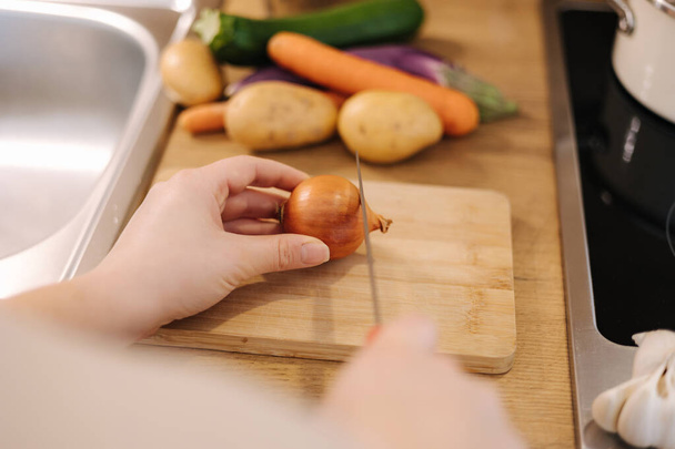 Foto de una mujer cortando una cebolla en una tabla de madera. Concepto de comida casera. Foto de alta calidad - Foto, imagen