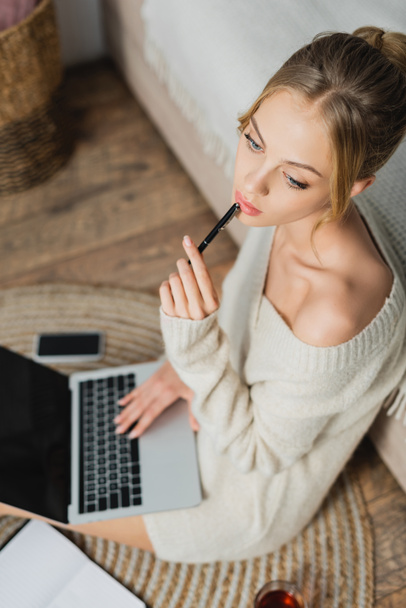 overhead view of thoughtful woman in sweater sitting with laptop in modern apartment  - Foto, Bild