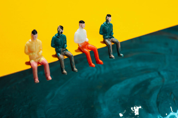 Toy people sitting on yellow background near water - 写真・画像
