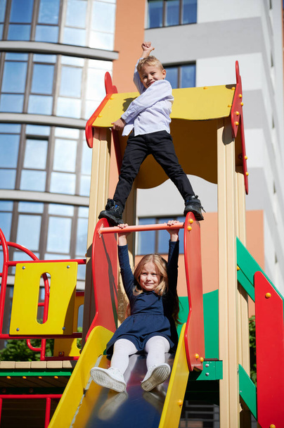 Alegre hermano y hermana se divierten en el patio de recreo. Niño y niña jugando en el patio moderno de la ciudad edificios residenciales de gran altura. - Foto, imagen