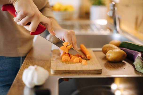 Close-up of female hand using knife and cutting carrot on wooden table. Home food concept . High quality photo - Fotó, kép