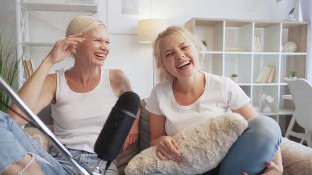 Talk show. Fun podcast. Home leisure. Two amused women laughing recording audio stream using microphone on sofa in living room. - Photo, image
