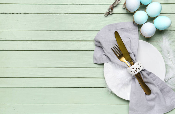 Juego de mesa con huevos de Pascua, cubiertos y plumas sobre fondo de madera verde - Foto, Imagen