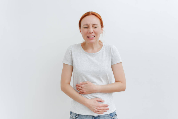 A young woman holds on to her stomach in pain. Digestive problems, gastrointestinal diseases concept. White backgroung. - Φωτογραφία, εικόνα