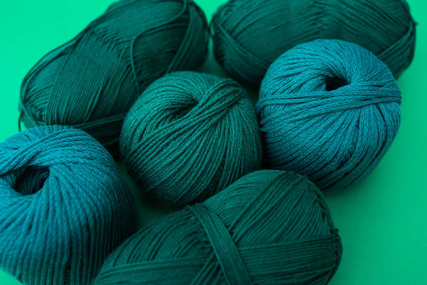 緑色の背景に異なる種類の糸を持つ糸の濃い緑色のボールの近いビュー。毛糸・綿糸. - 写真・画像