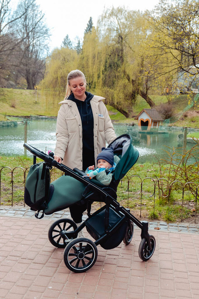 Happy boy sitting in a stroller with his mom in public park - Fotó, kép