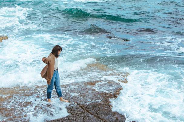 woman walking by rocky beach in wet jeans barefoot. summer sea vacation - Photo, image