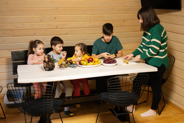 Mother with four children eat fruits in wooden country house on weekend. Mom cuts the yellow dragon fruit. - Foto, imagen