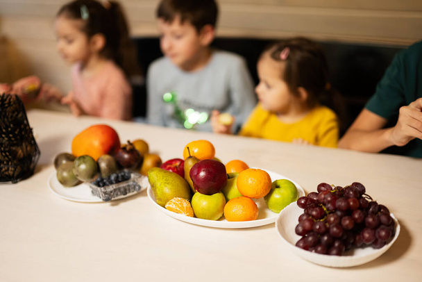 Four children eat fruits in wooden country house on weekend. - Foto, Imagen