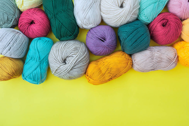 Layout of different balls and skeins of yarns, placed on bright yellow background with empty space below. Multicolored fibers for hand made work. - Фото, изображение