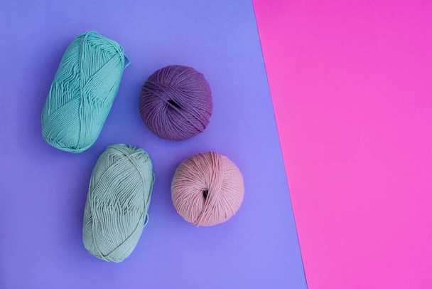 Balls of yarn - pink, violet, olive and blue on violet surface and empty space on the right in bright pink. Bright woolen yarns on bright background. - Foto, Imagen