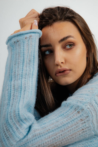 Vertical close up sad serious dark haired woman looking away and biting lips in blue woolen oversize sweater on white studio background. Depression after breaking up, mental health problem. Copy space - Foto, Imagem