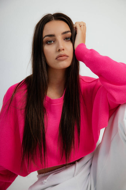 Vertical close up dark haired flirting, gorgeous woman with makeup in pink mini shirt pose like fashion model, look camera in white studio. Hair care and beauty treatment for skin. Copy space - Fotografie, Obrázek