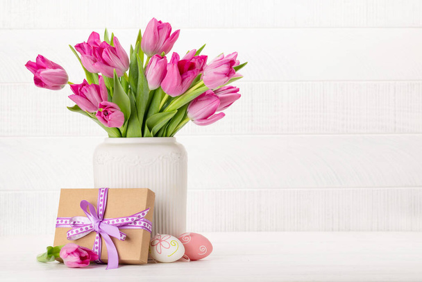 Fresh pink tulip flowers bouquet, easter eggs and gift box. On white wooden table with copy space - Photo, image