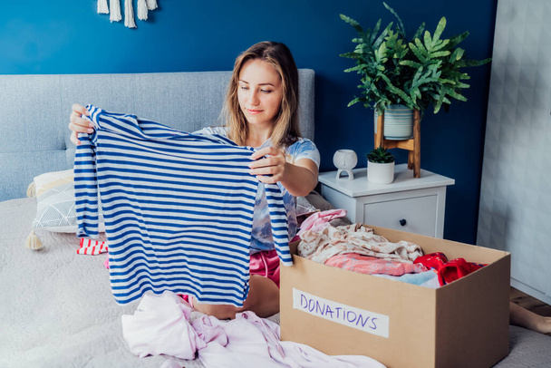 Woman selecting clothes from her wardrobe for donating to a Charity shop. Decluttering, Sorting clothes and Cleaning Up. Reuse, second-hand concept. Conscious consumer, sustainable lifestyle. - 写真・画像