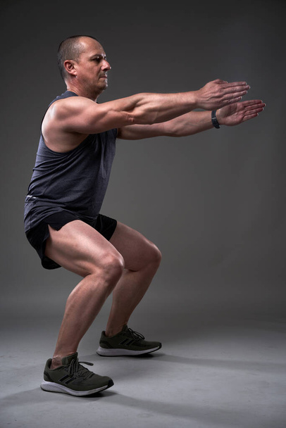maturo caucasico muscolare uomo in tee e pantaloncini facendo un allenamento di fitness su sfondo grigio - Foto, immagini