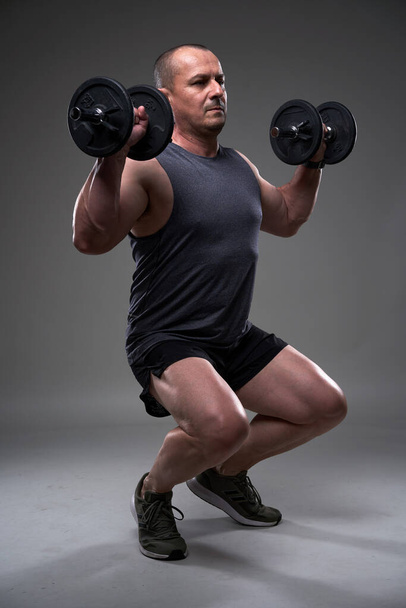 Mature caucasian muscular man in tee and shorts doing a fitness workout training on gray background - Fotoğraf, Görsel
