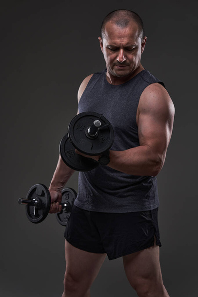 Mature caucasian muscular man in tee and shorts doing a fitness workout training on gray background - Фото, изображение