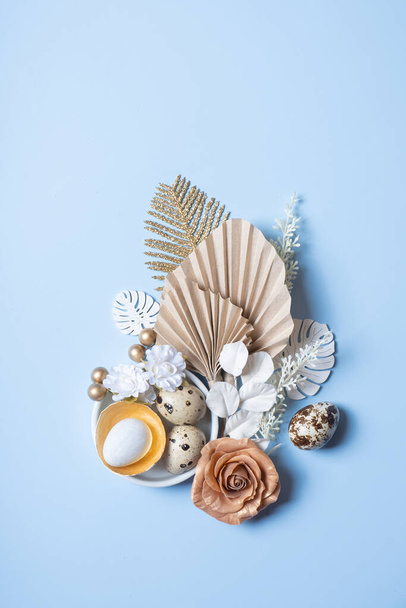 Modern kreatív kompozíció húsvéti tojással, pálmalevéllel és virágokkal felülnézetből. Húsvéti lakás. - Fotó, kép