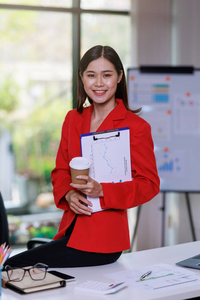 Concept of business office woman working,Businesswoman smile while working about her invesment plan with analyzing document and business investment graph data and holding coffee cup in workstation - Zdjęcie, obraz