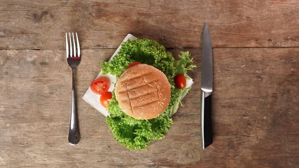 Vue du dessus d'un burger appétit contre une table en bois. Un couteau et une fourchette reposent sur la table. Espace de copie - Photo, image