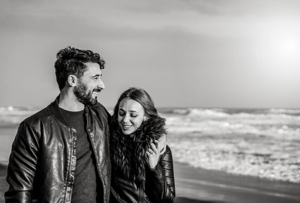 Fiatal pár kapcsolatban ölelkező és szerető egymást az első társkereső - Nő és férfi élvezi a szabadtéri szabadidős tevékenység a romantikus strand őszi szezonban - Fekete-fehér szerkesztés - Fotó, kép