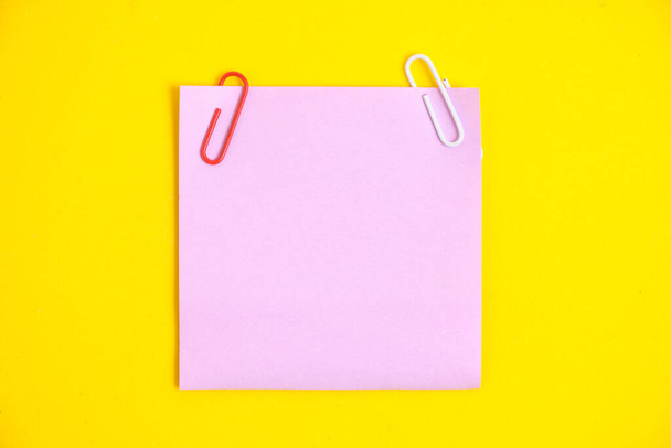 Lilac sticker for notes and paper clips yellow background - Φωτογραφία, εικόνα