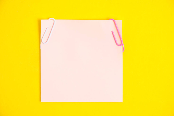 Ροζ αυτοκόλλητο για σημειώσεις και συνδετήρες κίτρινο φόντο - Φωτογραφία, εικόνα
