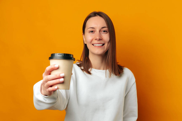 Prends mon café et goûte ça dit qu'une femme joyeuse donne sa tasse à la caméra. Studio tourné sur fond jaune. - Photo, image