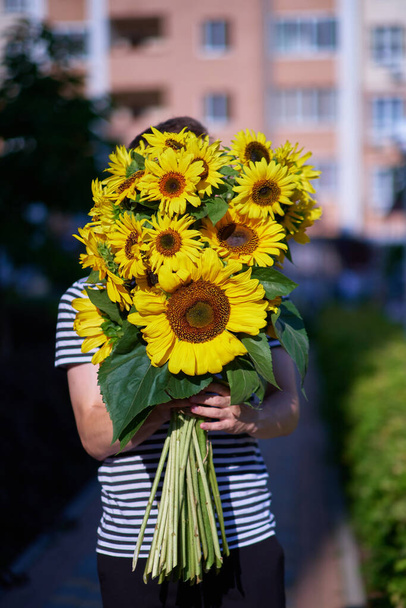 boeket gele zonnebloemen in handen van een onherkenbare man buiten. Patriottisch geschenk met liefde, dankbaarheid. Moederdag. Steun voor Oekraïne. Onafhankelijkheidsdag. Hoge kwaliteit foto - Foto, afbeelding