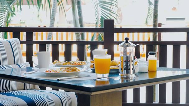 Fresh, healthy breakfast at tropical hotel restaurant. A variety of food, juices on palm trees background. Tropical breakfast at a luxurious hotel - Foto, Bild