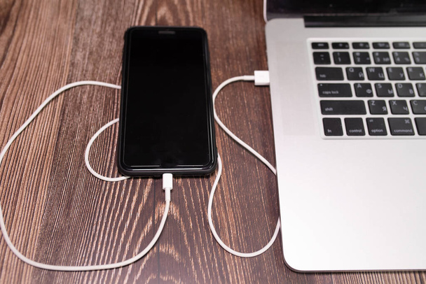 Sluit USB-kabel, kabellader, opladen, opgeladen en gegevensoverdracht van de mobiele telefoon, smartphone met een laptop aan  - Foto, afbeelding