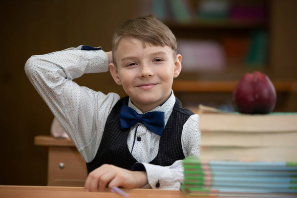 Iskolásfiú az asztalnál. Egy fiú az osztályteremben könyvekkel és egy almával. Középiskola. Vissza az iskolába.. - Fotó, kép