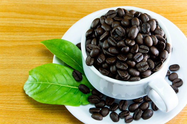 Zátiší pohár kávová zrna a listy kávy na dřevěný stůl - Fotografie, Obrázek