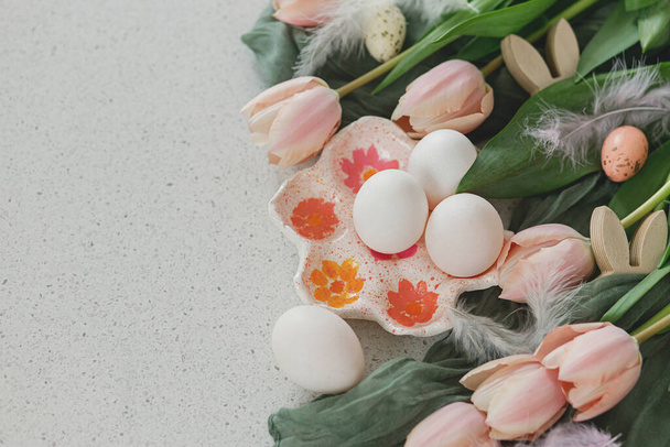 Belas tulipas, ovos naturais e decoração de coelho na mesa moderna. Páscoa elegante ainda vida com espaço de cópia. Feliz Páscoa! Suporte de ovo artesanal, tulipas rosa e orelhas de coelho de madeira - Foto, Imagem