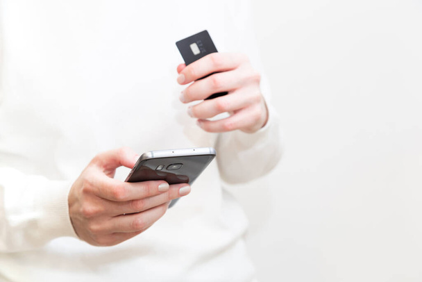 Lähikuva naisten käsissä luottokortilla ja käyttämällä älypuhelinta valkoisella taustalla. Nainen maksaa turvallisesti verkossa, pankkipalveluilla, tilaamalla verkkokaupasta. Verkkokauppa. - Valokuva, kuva