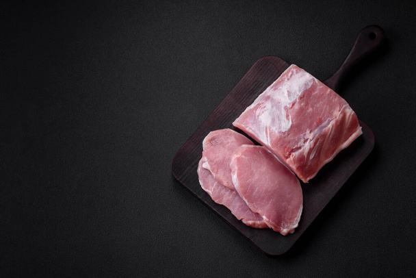 Fresh juicy pork on a wooden cutting board with spices and salt on a dark concrete background - Foto, imagen