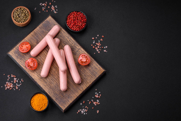 Boiled sausages on a wooden cutting board with tomatoes, spices and salt on a dark concrete background - Foto, immagini