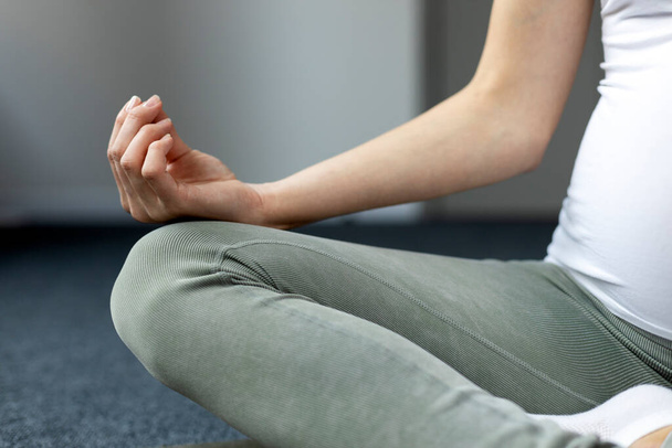 Gros plan de la femme enceinte méditant, pratiquant le yoga assis sur la pose de lotus à la maison, foyer sélectif. Yoga de grossesse et concept de fitness - Photo, image