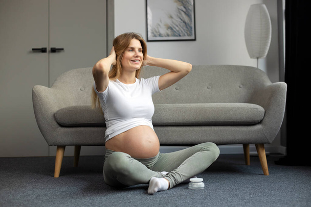 Bela mulher grávida sorrindo fazendo exercícios, meditação, sentada em posição de lótus no chão. Conceito de ioga de gravidez  - Foto, Imagem