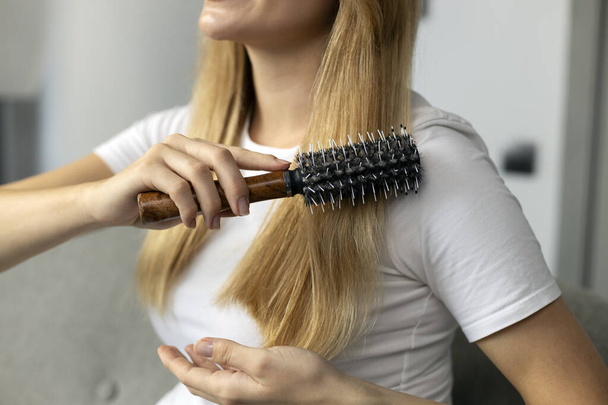 Closeup of woman hand brushing her hair at home, selective focus. Beauty and hair care concept  - Valokuva, kuva