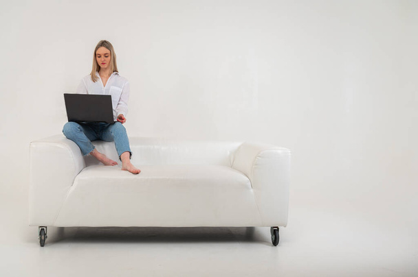 junges hübsches Mädchen sitzt auf Laptop sitzt auf Sofa isoliert auf hellem Hintergrund schöne Mädchen einkaufen oder chatten online auf sozialen Netzwerken Spaß beim Ansehen von Film - Foto, Bild