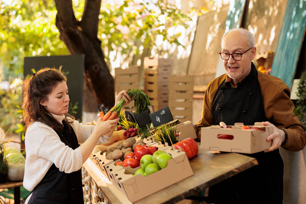 Ein Team von Verkäuferinnen und Verkäufern älterer Männer verkauft gesunde Produkte vom Bauernhof und bereitet einen Stand mit Obst und Gemüse für die Kunden vor. Bauern arbeiten auf dem lokalen Markt, um Kunden mit Bioprodukten zu helfen. - Foto, Bild