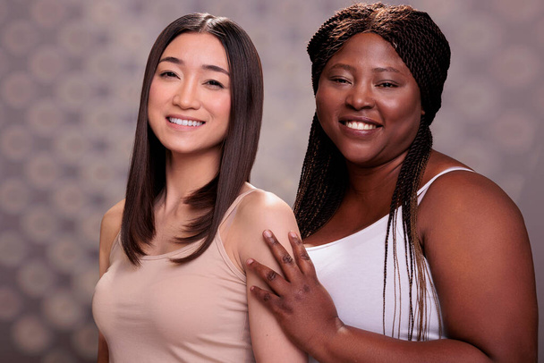 Hermosas mujeres jóvenes con diferentes tipos de cuerpo y etnia posando juntos retrato. Asiático y africano americano confiado cuerpo positivo belleza modelos usando casual tops - Foto, Imagen