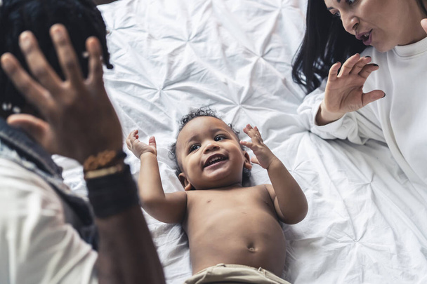 Afroamerikkalainen pikkupoika makaa sängyllä ja leikkii vanhempiensa kanssa vapaa-ajalla. Laadukas kuva - Valokuva, kuva